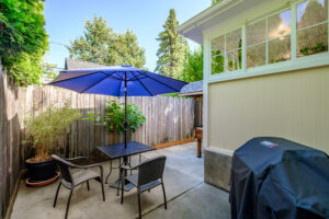 Back patio seating with a covered gas grill against the fence and greenery